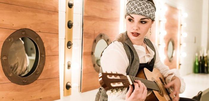 An actress playing a pirate who is playing guitar in front of portholes 